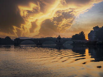 Wolken über dem Fluss Rhone bei Sonnenuntergang mit Silhouette der Bogenbrücke im Hintergrund, Vaucluse, Frankreich - HAMF00822