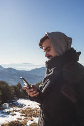 Porträt eines Mannes, der mit seinem Smartphone im Schnee eine Nachricht verschickt - MGRF00163
