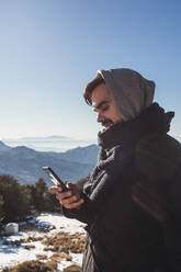 Portrait of a man sending a message with his smartphone in the snow - MGRF00163