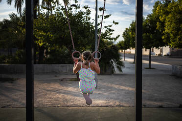 Girl hanging on gymnastic rings on playground at park - AMPF00024