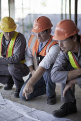 Male architect explaining plans to construction workers on site - AJOF01028