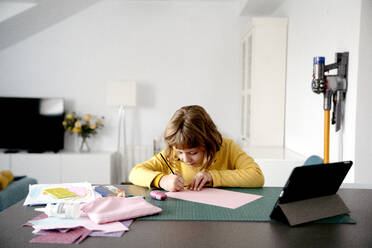 Blond girl drawing on paper while watching tutorial on digital tablet at home - AMPF00028