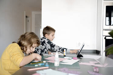 Siblings doing art and craft while using digital tablet at home - AMPF00029