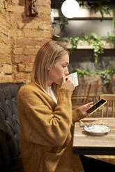 Junge Frau trinkt Kaffee und benutzt ihr Smartphone in einer Cafeteria - VEGF03877