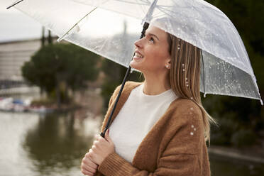 Glückliche Frau schaut nach oben und hält einen Regenschirm während der Regenzeit - VEGF03891