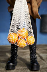 Junge Frau hält Orangen in einer wiederverwendbaren Tasche, während sie auf dem Fußweg steht - VEGF03900
