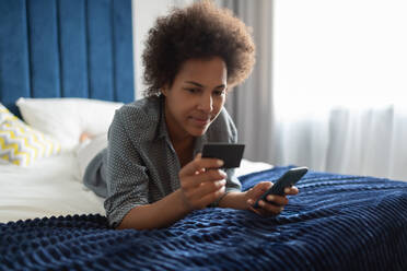 African American woman making online purchases on bed - CAVF93126