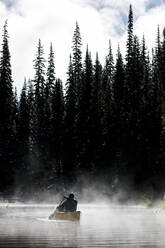 Rückansicht eines Mannes beim Kanufahren auf einem See gegen Nebel und Bäume - CAVF93137