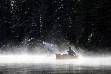 Mann beim Bootfahren auf einem abgelegenen See an einem nebligen Herbsttag - CAVF93142