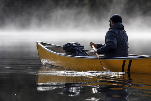 Bärtiger Mann paddelt bei nebligem Wetter auf einem See - CAVF93153