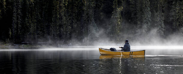 Mann paddelt Kanu auf einem See mit Nebel und Dunst an einem sonnigen Tag im Wald - CAVF93154