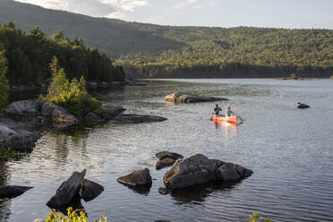 Ehepaar paddelt mit rotem Kanu zwischen Felsen auf einem See in der Wildnis von Maine - CAVF93159