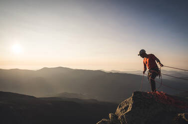 Mann beim Sichern mit Kletterseilen bei Sonnenaufgang in den Bergen - CAVF93183