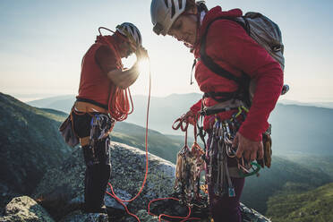 Mann und Frau sortieren Kletterausrüstung am frühen Morgen in den Bergen - CAVF93184