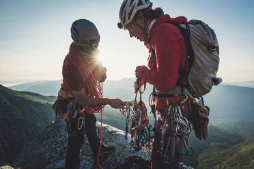 Mann und Frau sortieren Kletterausrüstung am frühen Morgen in den Bergen - CAVF93185
