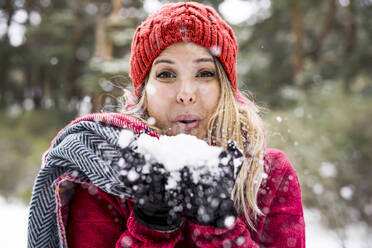 Porträt einer glücklichen jungen Frau, die im Winter mit Schnee spielt und Schneeflocken in die Kamera bläst, Kopierraum - CAVF93193