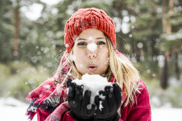 Porträt einer glücklichen jungen Frau, die im Winter mit Schnee spielt und Schneeflocken in die Kamera bläst, Kopierraum - CAVF93194