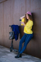 Junge Frau benutzt Smartphone in der Nähe der Wand und des Rollers - CAVF93219
