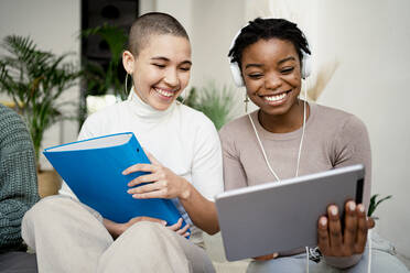 Smiling businesswoman using digital tablet sitting by female colleague at home - RCPF00677