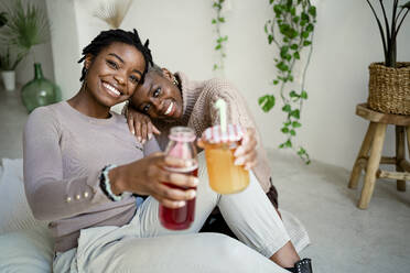 Lächelnde Freunde mit Saft trinken zu Hause sitzen - RCPF00692