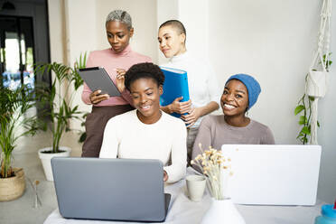 Happy female colleagues working on laptop at home - RCPF00713