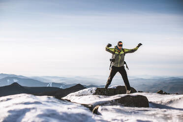 Mann mit Kamera springt von eisigem Felsen auf Berggipfel im Winter - CAVF93294