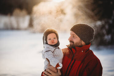 Papa und schöne Baby draußen im Schnee im Winter während goldenen Sonnenuntergang - CAVF93331