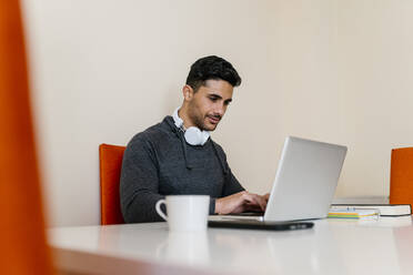 Young man with headphone using laptop while sitting at table in living room - EGAF01738