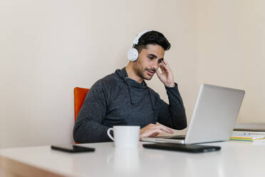 Young man listening music while using laptop in living room - EGAF01742