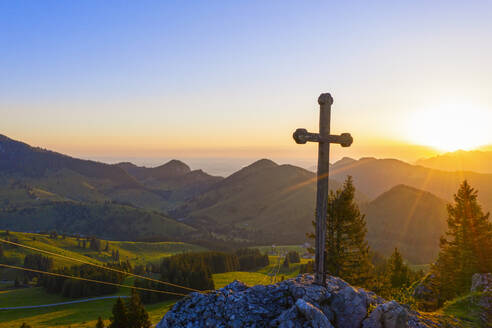 Rising sun illuminating Christian cross standing at summit of Sudelfeldkopf mountain - SIEF10093