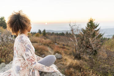 Frau mit lockigem braunem Haar übt Yoga bei Sonnenuntergang - AKLF00036