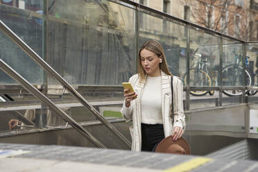 Schöne Frau, die ein Mobiltelefon benutzt, während sie von einer U-Bahn-Station aufsteigt - VEGF03911