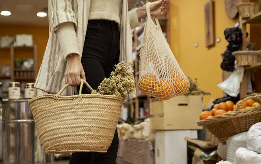 Kräuter und Orangenfrüchte in einer Tüte, die von einer Frau im Geschäft gehalten wird - VEGF03923