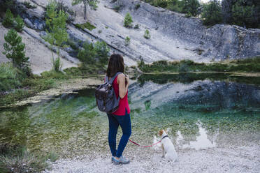 Woman with back standing by dog at lake - EBBF02465