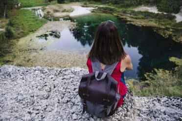 Woman with backpack sitting on rock at lake - EBBF02466