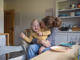 Fröhliche Mutter umarmt Tochter in der Küche zu Hause - LAF02681