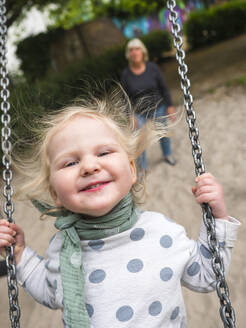 Cheerful girl on swing while grandmother standing at park - LAF02682