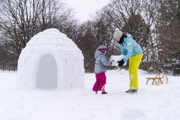 Mother helping daughter to carry snow block at park - DIGF14519