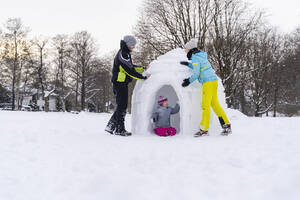 Father and mother helping daughter to build igloo in snow at park - DIGF14525