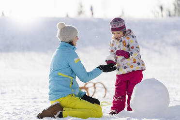 Mother helping daughter in making snowman at park - DIGF14526