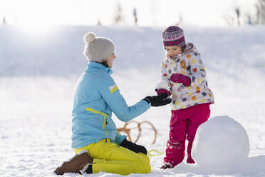 Mutter hilft Tochter beim Schneemannbau im Park - DIGF14526