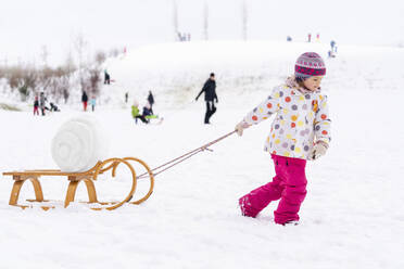 Mädchen in warmer Kleidung, das einen Schlitten auf Schnee im Park zieht - DIGF14527
