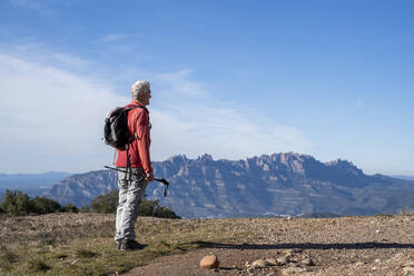 Älterer Mann mit Rucksack und Wanderstock mit Blick auf den Montserrat, während er auf einem Berg in Sant Llorenc del Munt i l'Obac, Katalonien, Spanien steht - AFVF08154