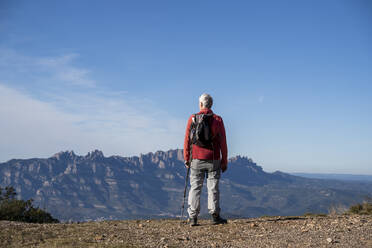 Älterer Wanderer mit Rucksack bewundert die Aussicht auf den Montserrat, während er auf dem Berg bei Sant Llorenc del Munt i l'Obac, Katalonien, Spanien steht - AFVF08155