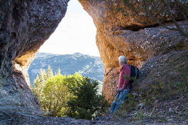 Älterer Mann mit Rucksack, der die Aussicht betrachtet, während er sich auf einem Felsen in Sant Llorenc del Munt i l'Obac, Katalonien, Spanien, ausruht - AFVF08158