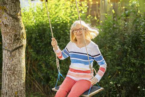 Fröhliche ältere Frau beim Schaukeln im Garten, lizenzfreies Stockfoto