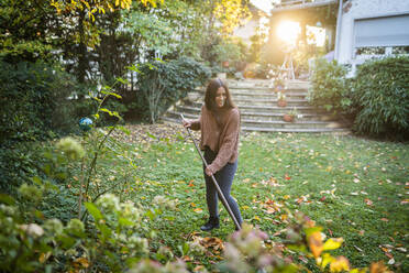 Glückliche Frau, die den Garten mit einem Besen im Hinterhof fegt - AKLF00052