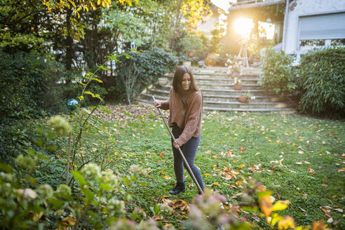 Happy woman sweeping garden with broom in back yard - AKLF00052