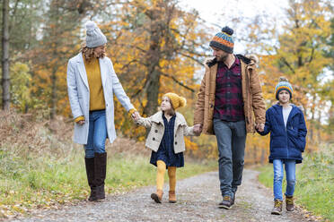 Family holding hands while walking on footpath at forest during autumn - WPEF04066