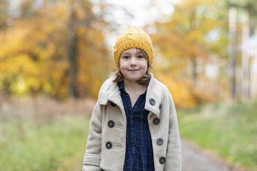 Cute girl wearing knit hat and jacket staring while standing in forest - WPEF04073